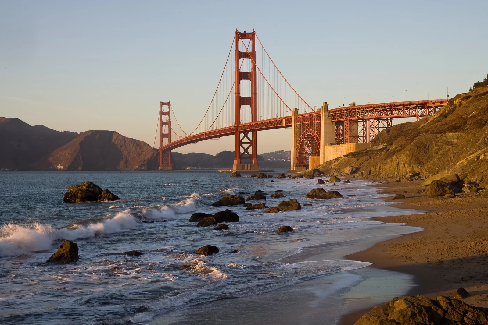Golden Gate Bridge above the surf and sand at Baker Beach in warm evening light